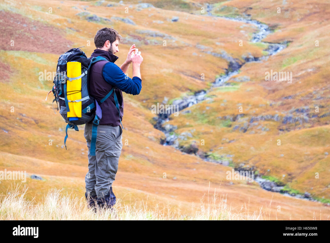 Maschio nella sua metà anni venti passeggiata in collina nel distretto del lago, prendendo una foto con uno smart phone Foto Stock