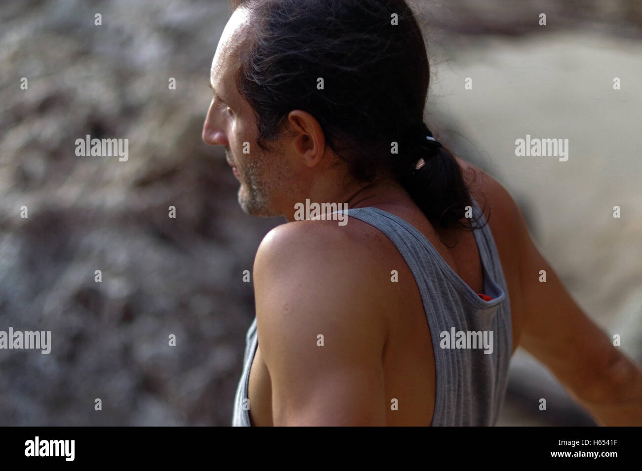 Ritratto di un uomo di mezza età con capelli lunghi, veduta laterale esterno con rock sullo sfondo Foto Stock