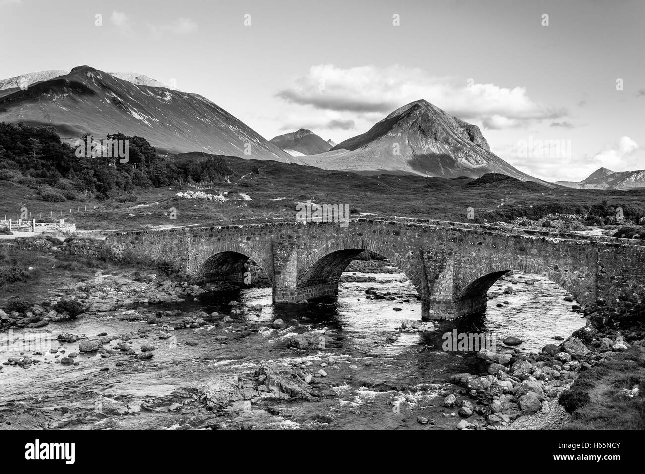 Famoso vecchio mattone Vintage ponte che attraversa il fiume in Sligachan, Isola di Skye in Scozia con le colline in lontananza - bianco e nero Foto Stock
