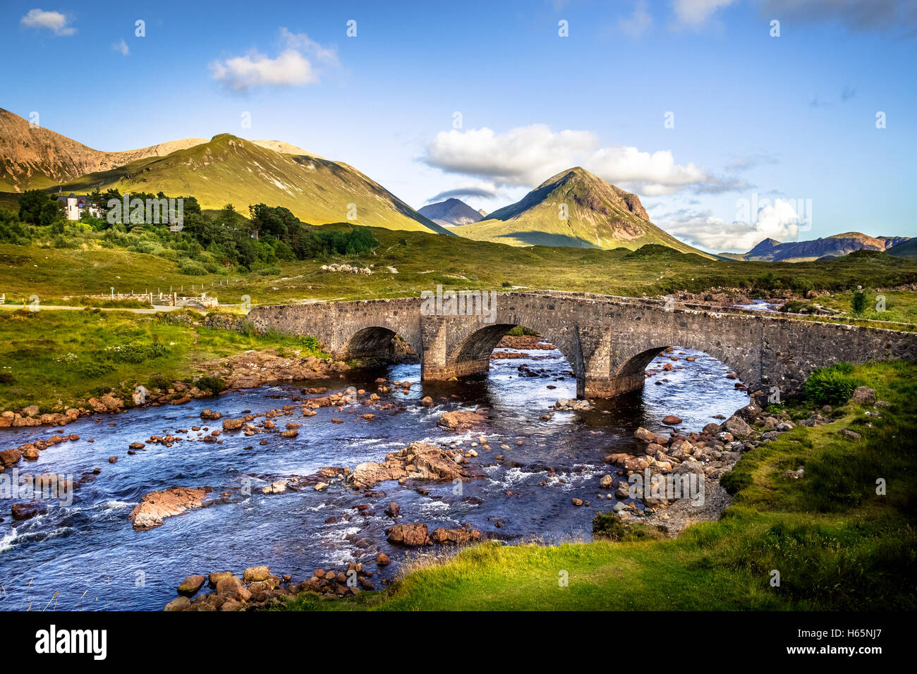 Famoso vecchio mattone Vintage ponte che attraversa il fiume in Sligachan, Isola di Skye in Scozia con le colline di distanza Foto Stock