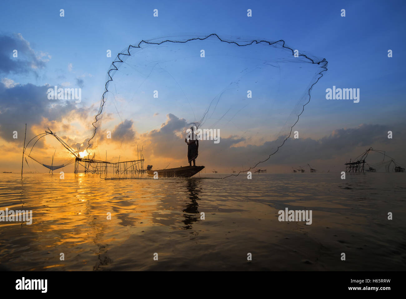 Pescatore sulla barca di legno di una rete di colata per la cattura del pesce. Fisherman gettando la pesca net durante il Sunrise in Pak Pra, Phatthalung Foto Stock