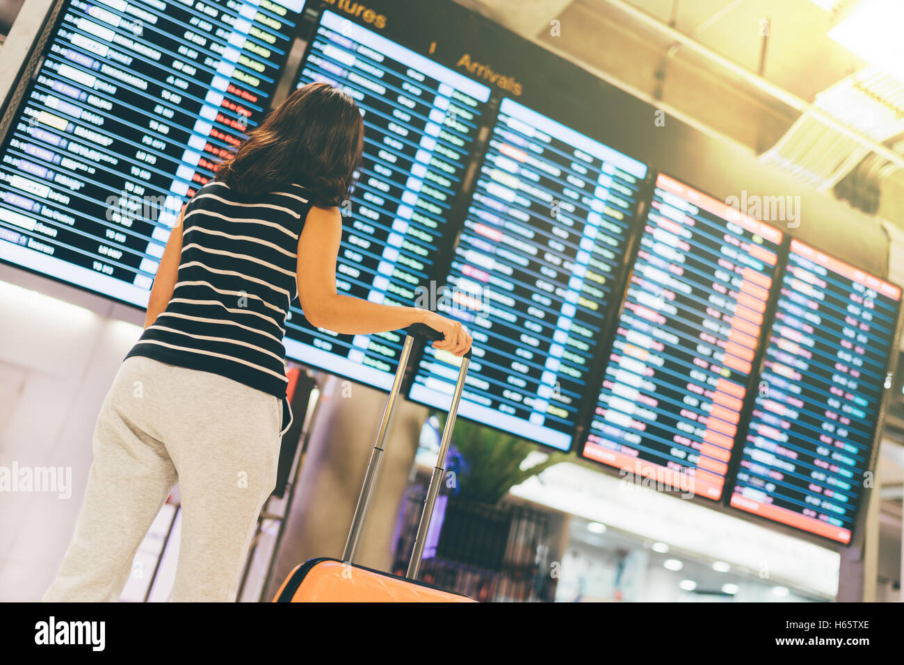 Donna asiatica traveler guardando le informazioni di volo lo schermo in un aeroporto, tenendo la valigia, viaggi o il concetto di tempo, una luce calda Foto Stock