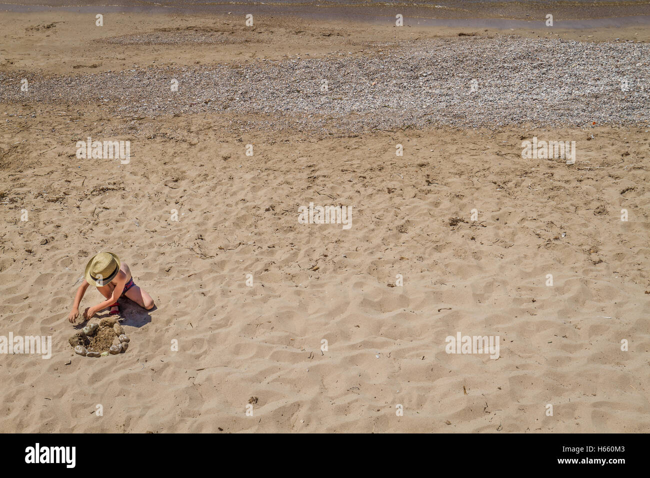 Fanciullo giocando con pietre e sabbia sulla spiaggia sulla giornata di sole Foto Stock