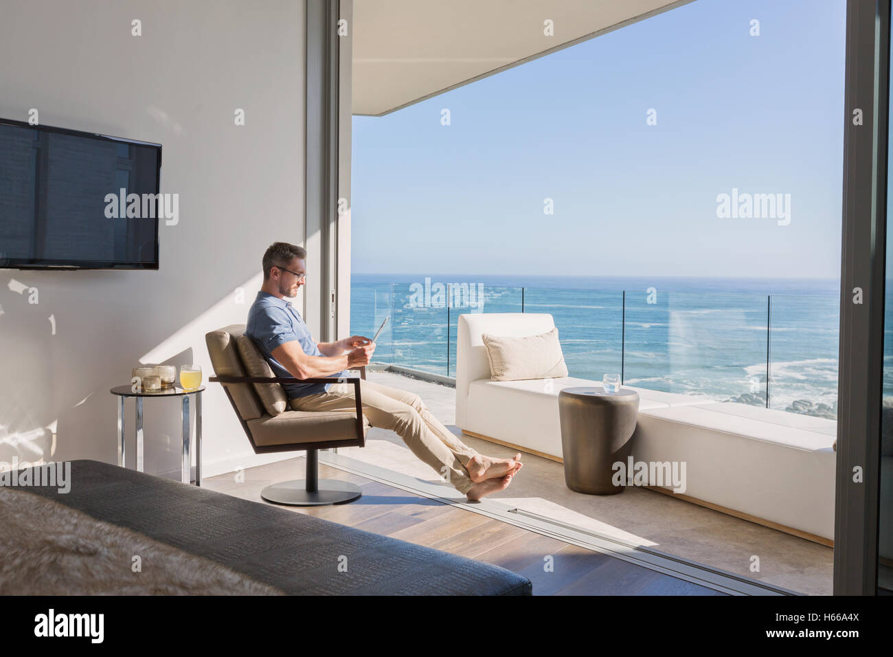 Uomo con tavoletta digitale che si affaccia soleggiato vista oceano Foto Stock