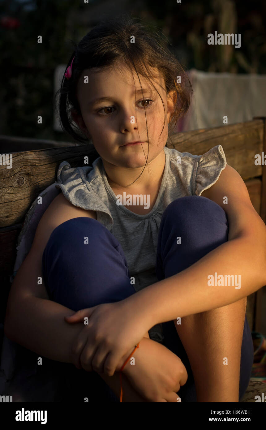 A sette anni di età ragazza triste seduto in una sedia in campagna in una luce della sera. Foto Stock
