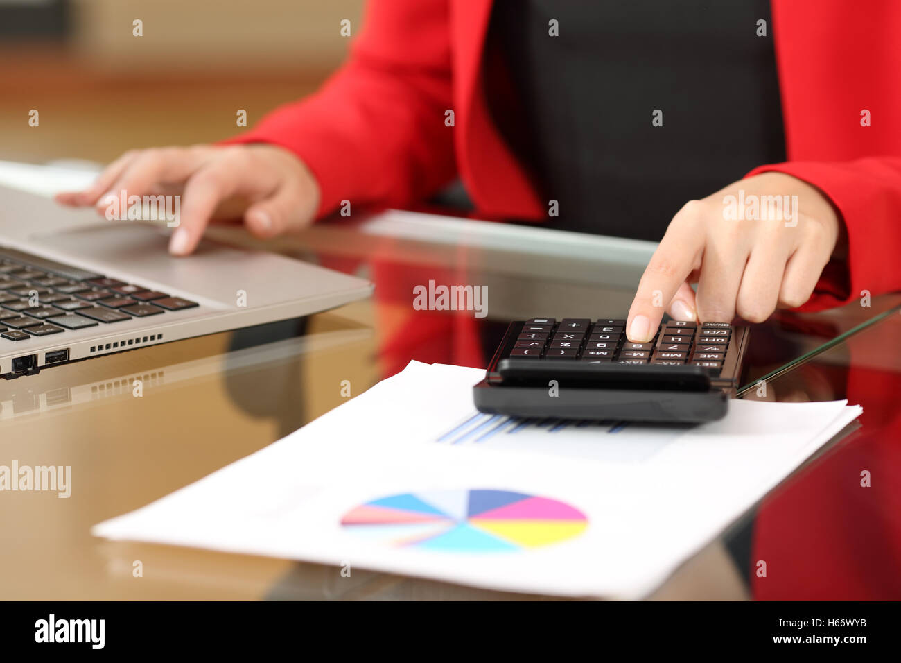 Primo piano di una imprenditrice mani contabilità con un nero calcolatrice e un laptop seduto in un desktop in ufficio Foto Stock