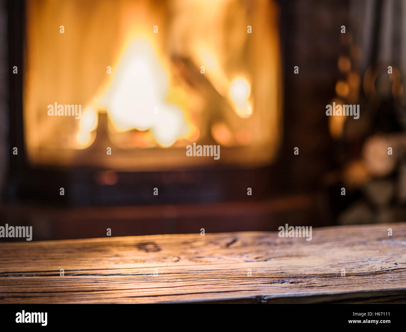 Vecchio tavolo in legno e camino con fuoco caldo sullo sfondo. Foto Stock