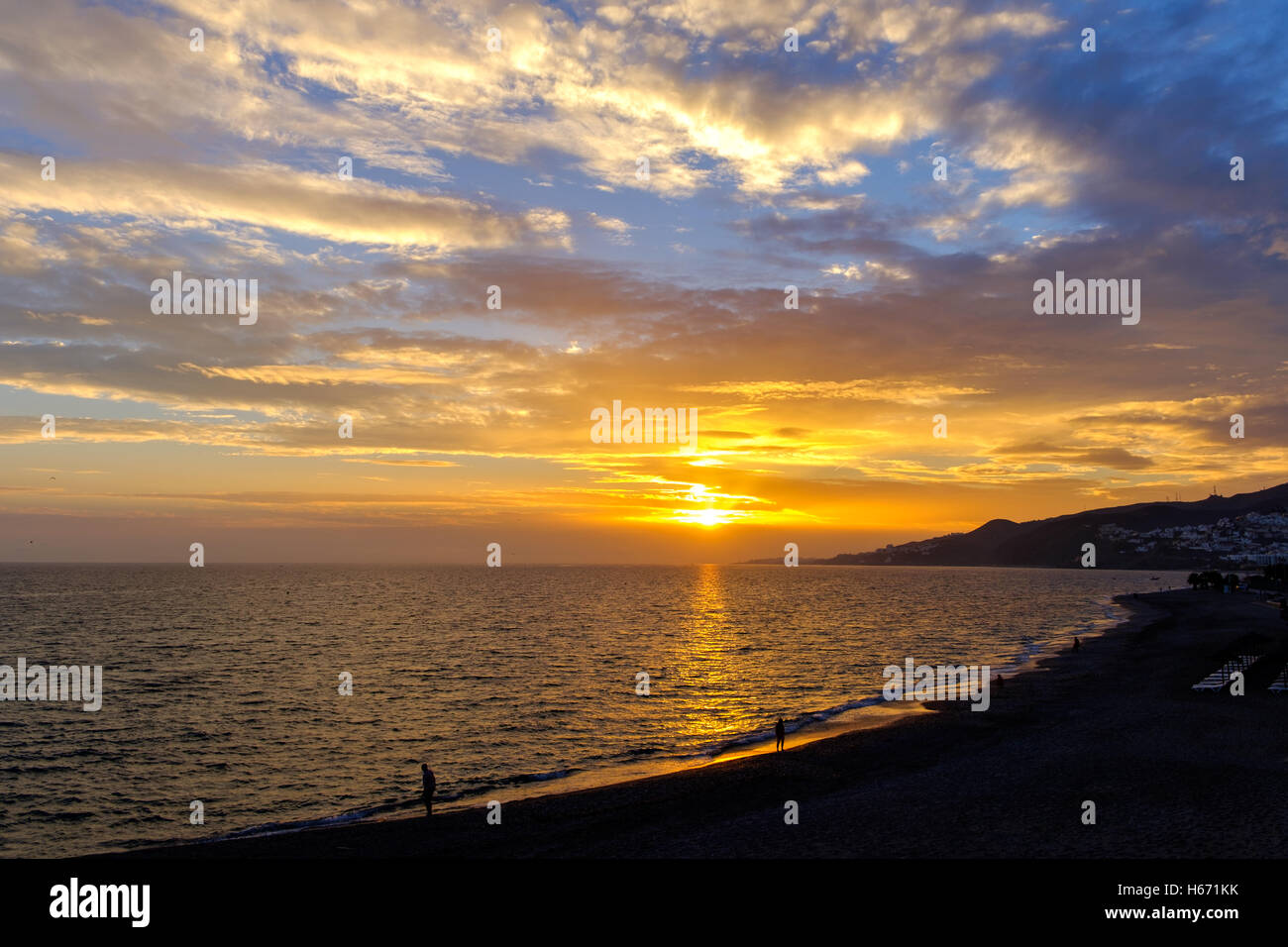Un bellissimo tramonto su un poco nuvoloso sky prese attraverso una spiaggia e mare Foto Stock