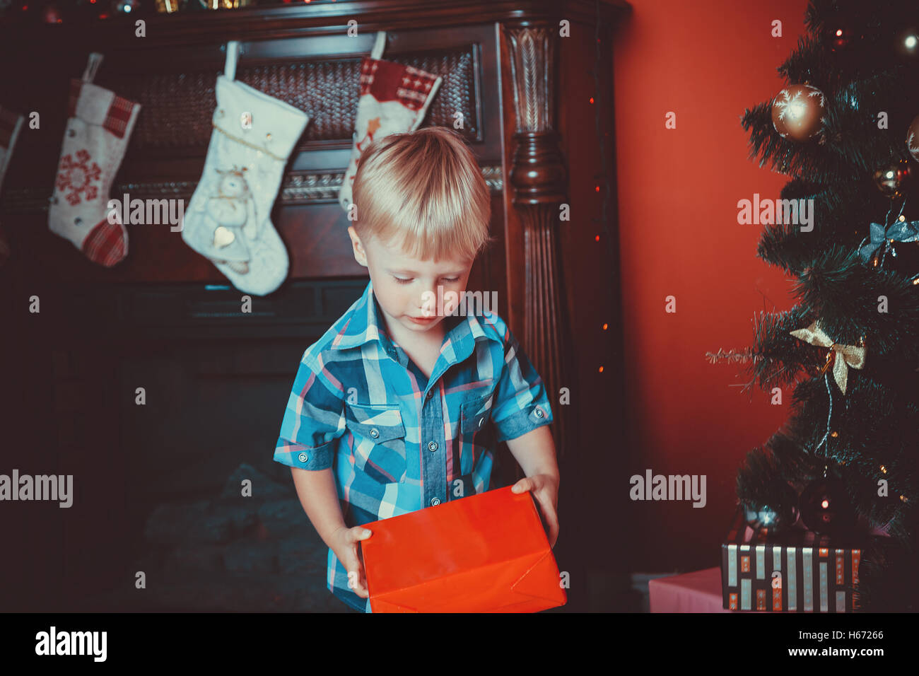 Bel ritratto di un ragazzino con un regalo in mano nel nuovo anno camera con un albero di natale. L'idea per cartoline. focu morbido Foto Stock