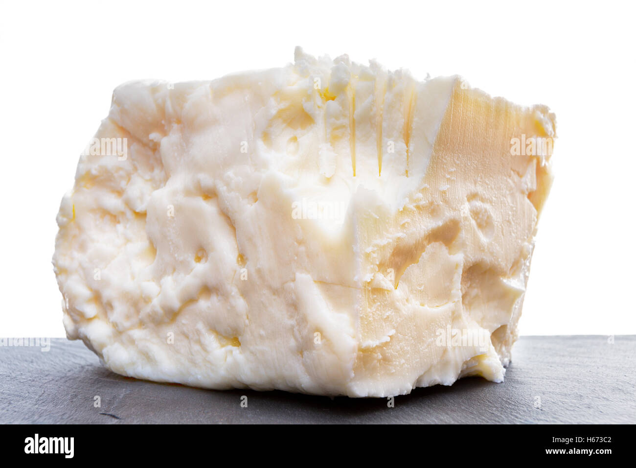 Lato Vista ravvicinata sul pieno di grasso il formaggio feta con dentellature e segni di taglio sulla superficie scura su sfondo bianco Foto Stock