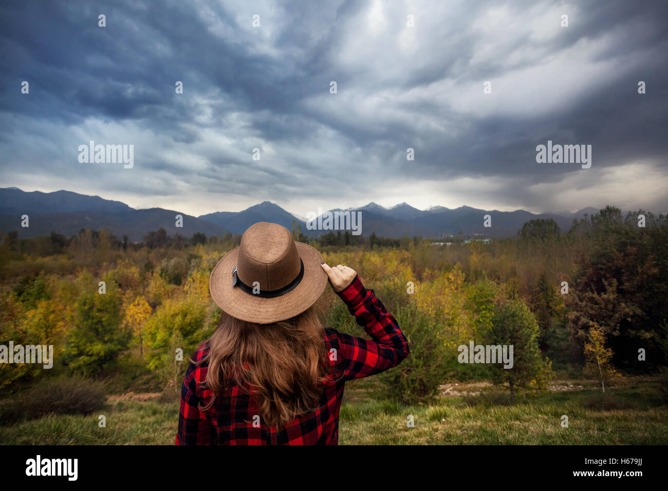 Woman in Red controllato shirt e hat cercando in autunno la foresta e le montagne sullo sfondo. Concetto di viaggio. Foto Stock