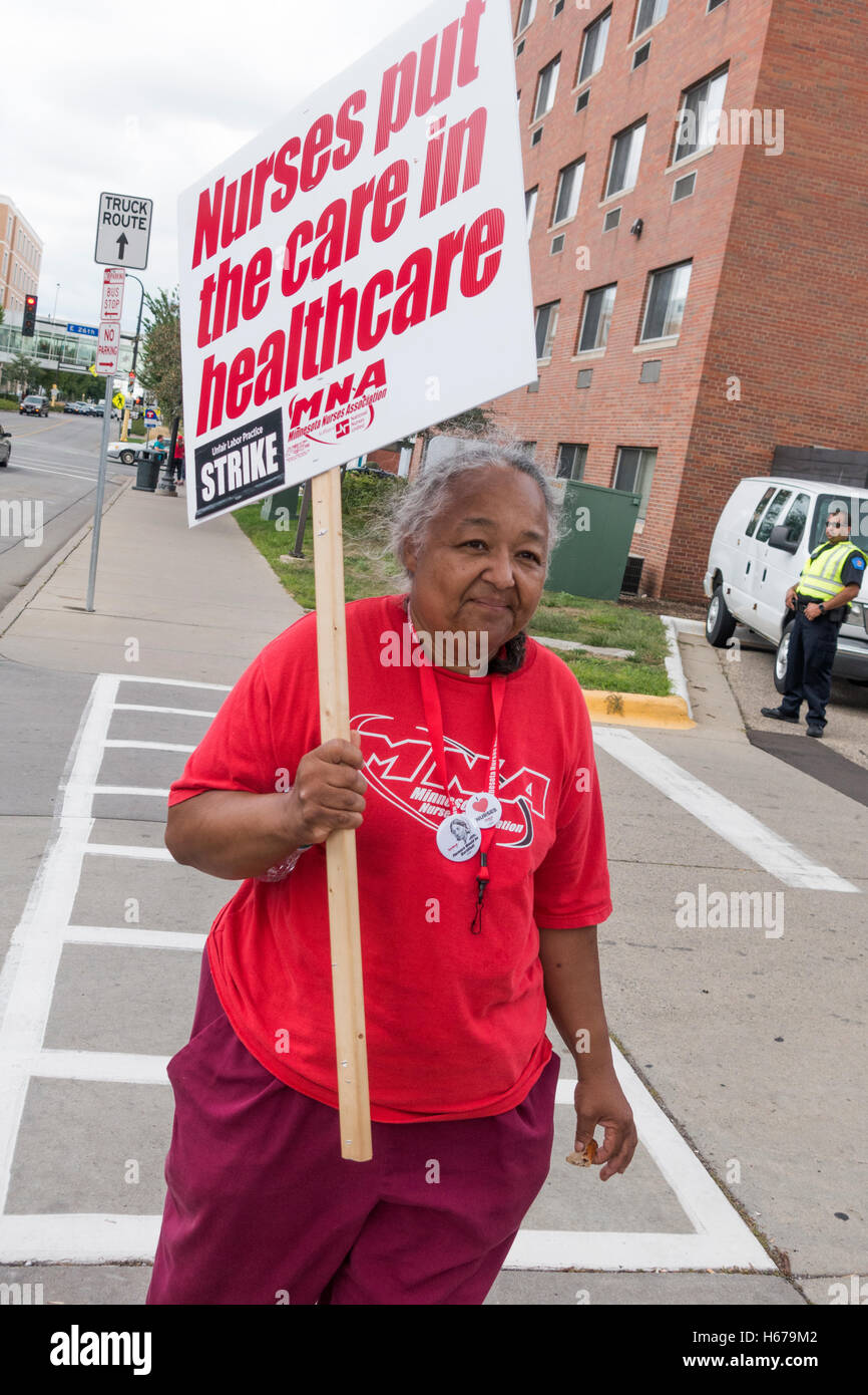 Matura donna etnica infermiere targhetta portante protestando nuovi benefici per la salute al pacchetto salute Allina Minneapolis Minnesota MN USA Foto Stock