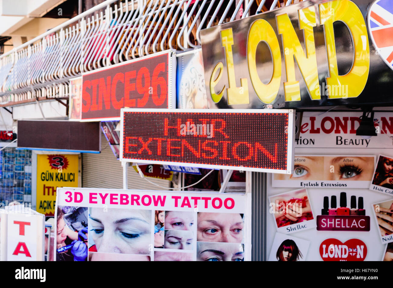 Un sacco di segni al di fuori di un parrucchiere pubblicità le estensioni di capelli, 3D sopracciglio tattoo, smalto per unghie ecc. Foto Stock