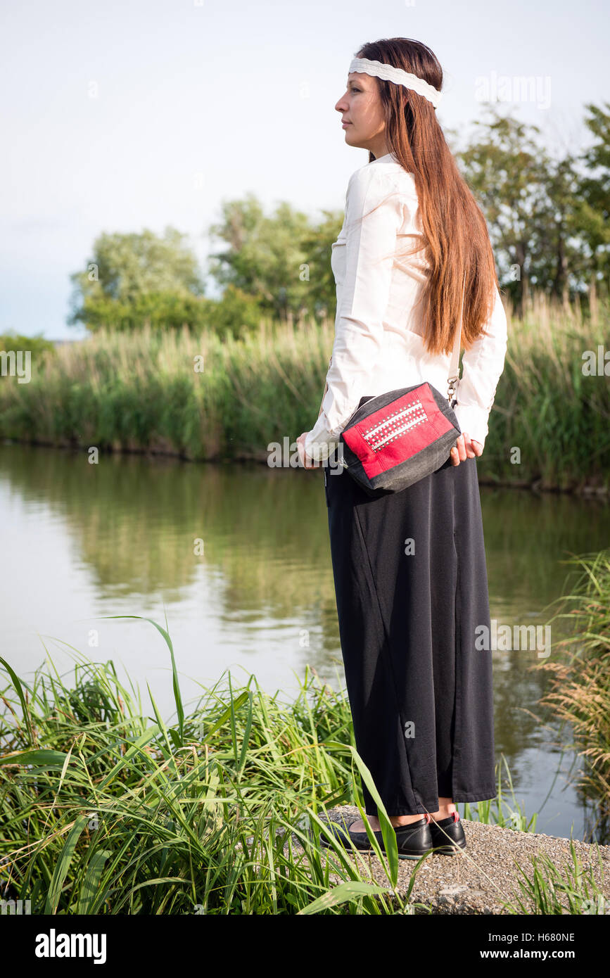 Ritratto di giovane donna hippie con borsetta in piedi vicino al lago Foto Stock