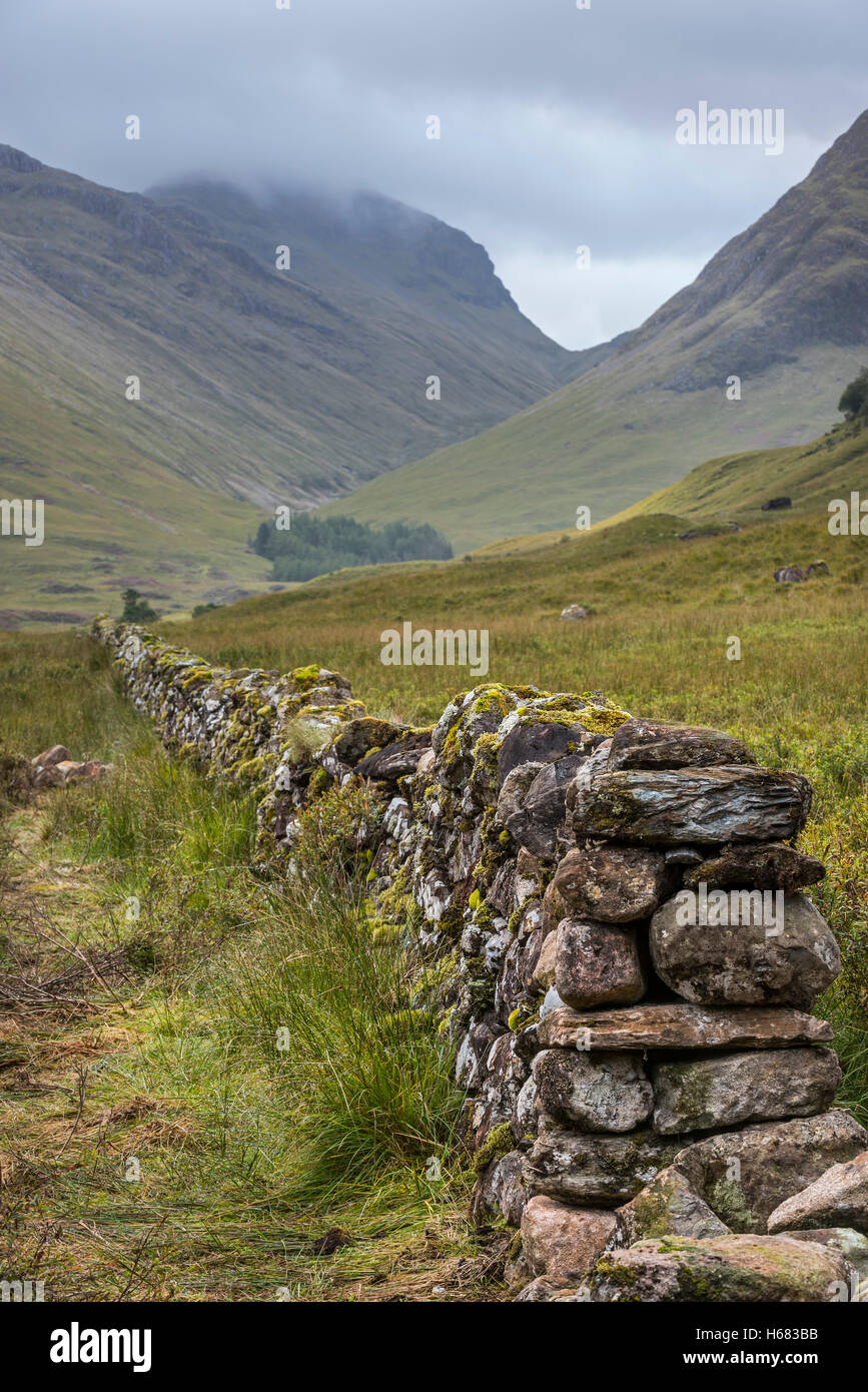 Asciugare vecchio muro di pietra nella brughiera che conduce alla montagna Bidean nam Bian e tre sorelle di Glen Coe, Highlands scozzesi, Scozia Foto Stock