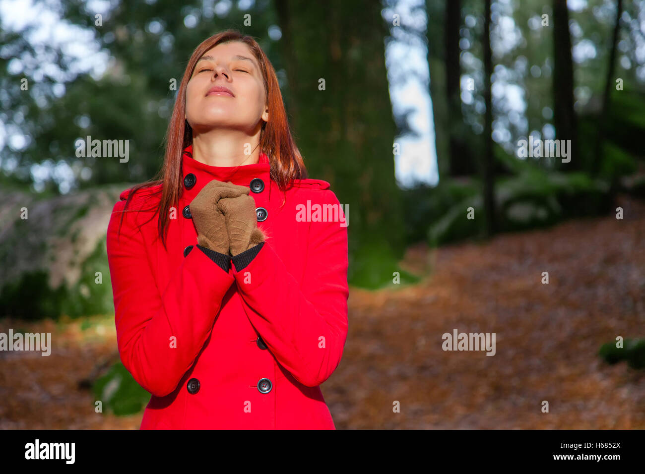 Donna godendo il calore del sole d'inverno su una foresta che indossa un soprabito rosso Foto Stock