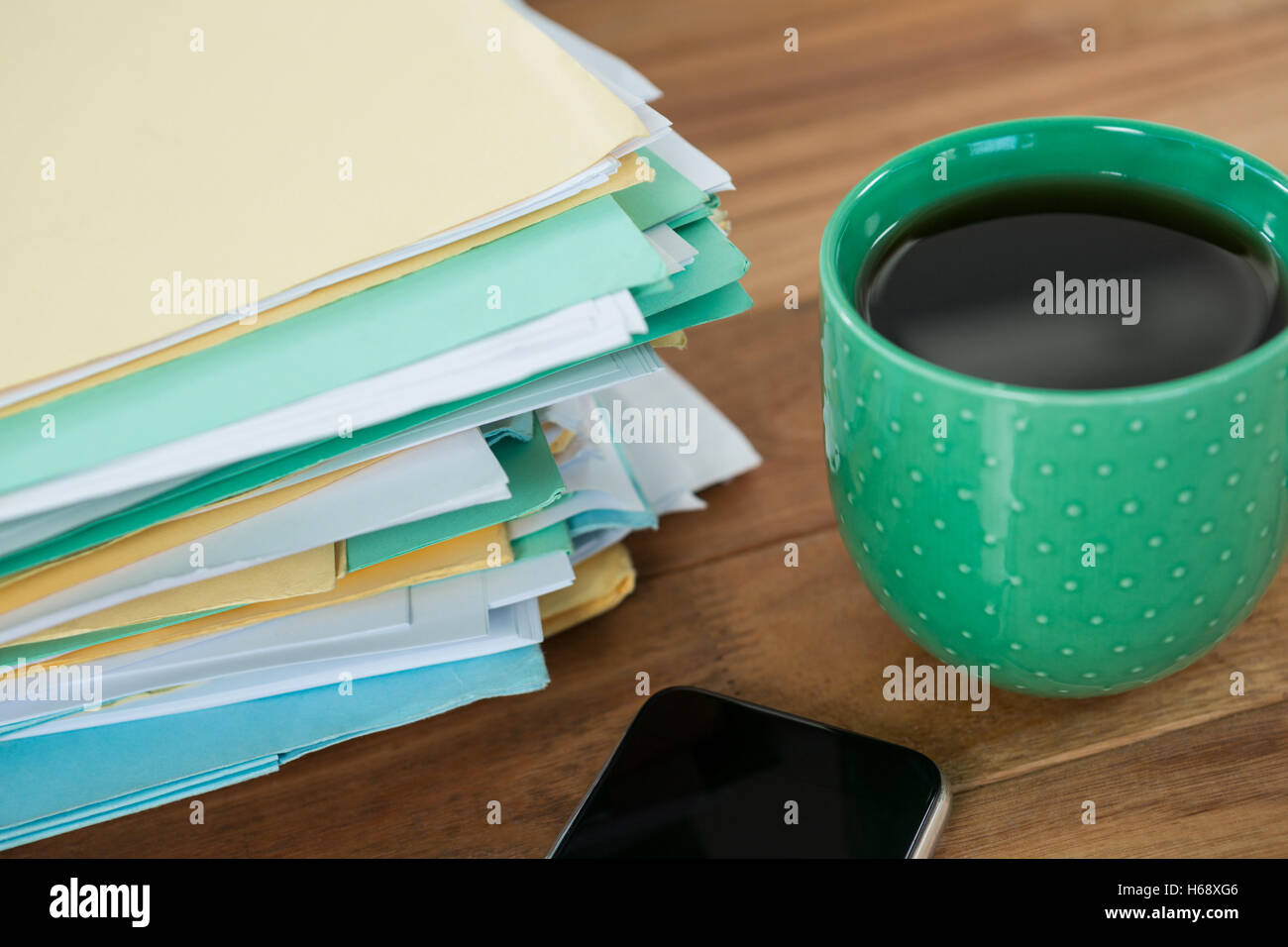 Tazza da caffè, telefono cellulare e file impilati sul tavolo Foto Stock
