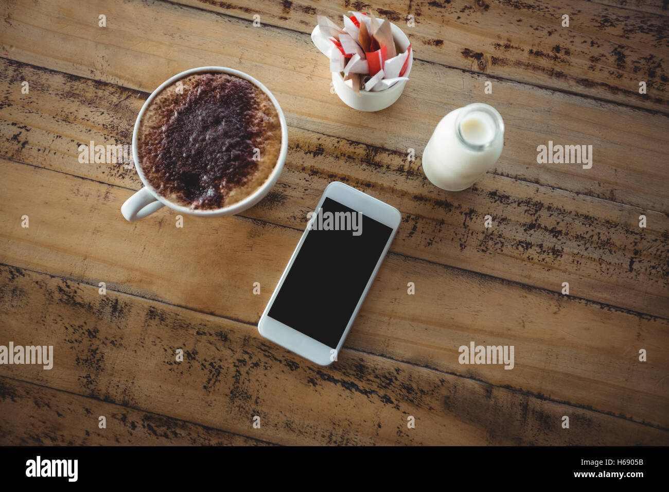 Tazza da caffè, telefono cellulare e bottiglia di latte su un tavolo Foto Stock