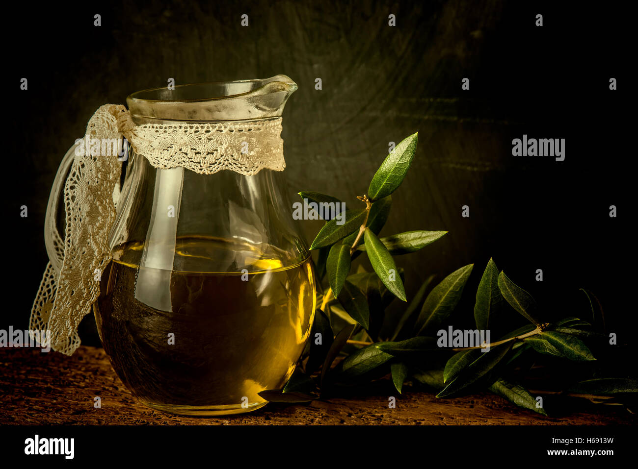 Olio extra vergine di oliva vasetto in vetro e foglie su sfondo rustico Foto Stock