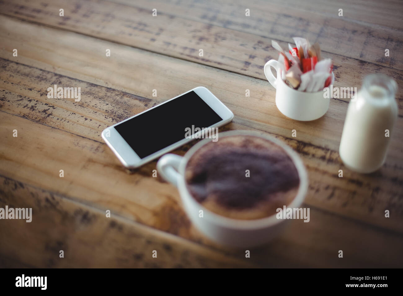 Close-up della tazza di caffè con il telefono cellulare e bottiglia di latte Foto Stock