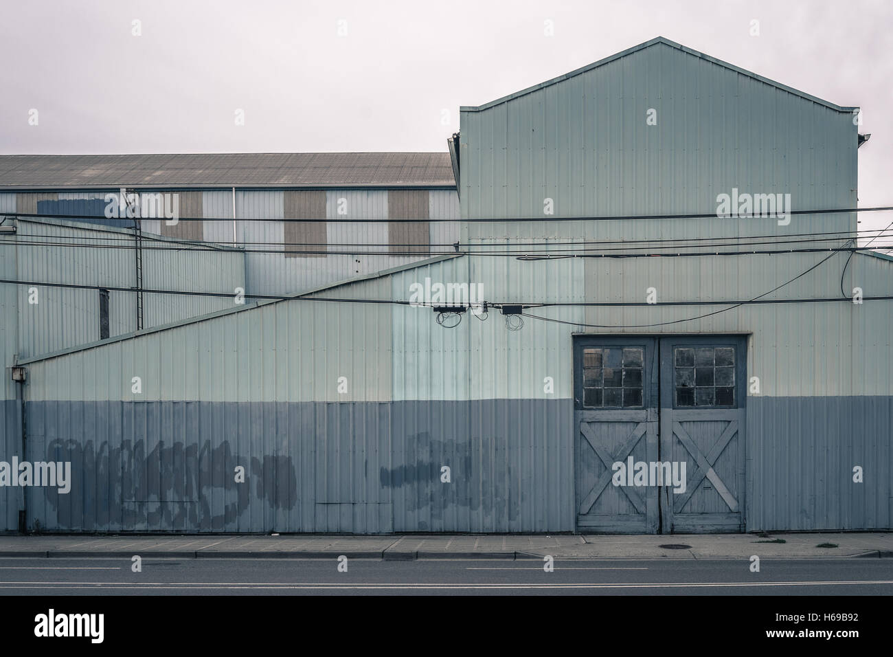 Il vecchio magazzino dipinto di blu e grigio con graffiti pulite e belle porte e coperto di windows su di una superficie piana, giorno nuvoloso Foto Stock