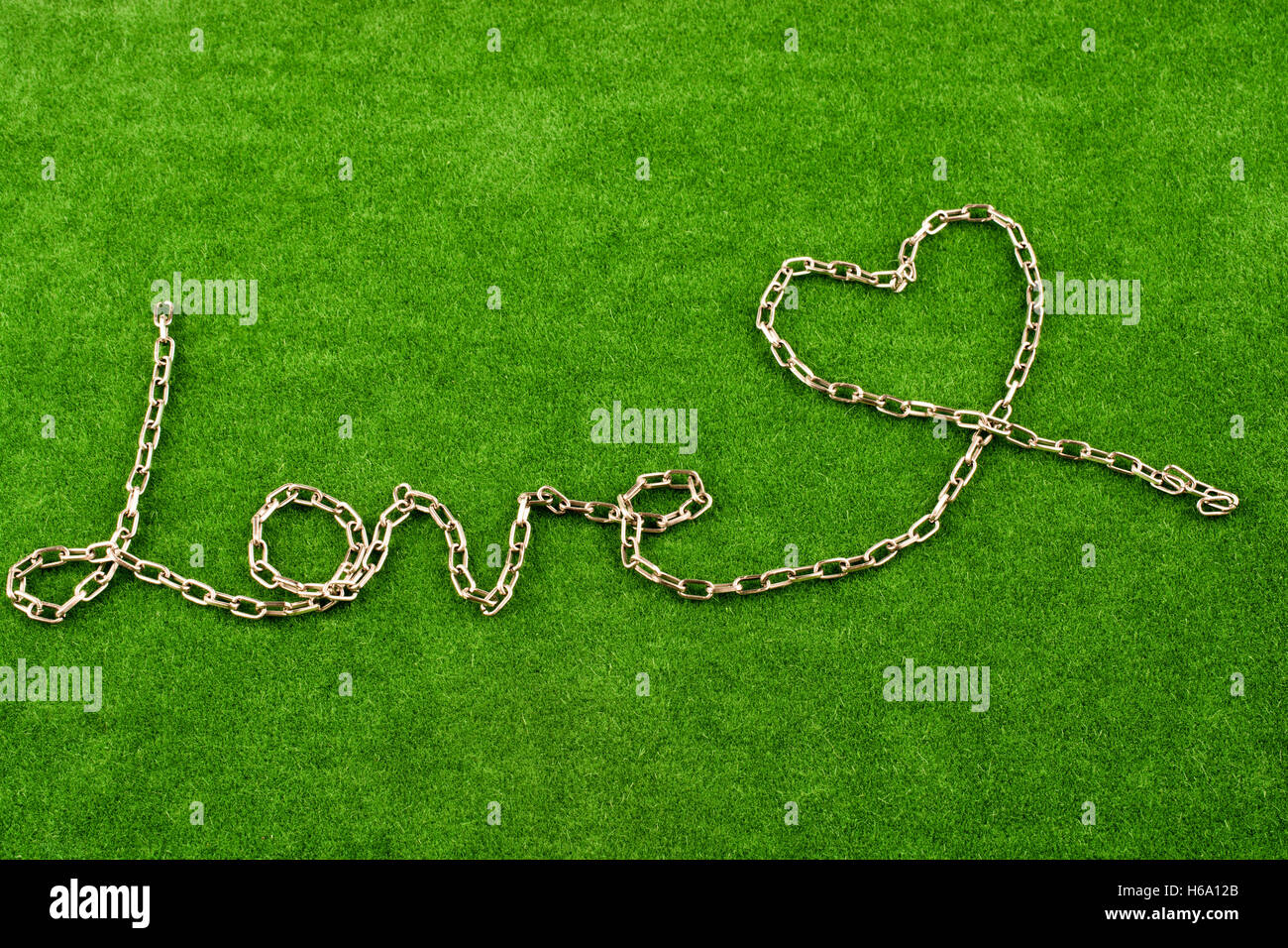 Forma di catena a forma di cuore e la parola amore sull'erba Foto Stock