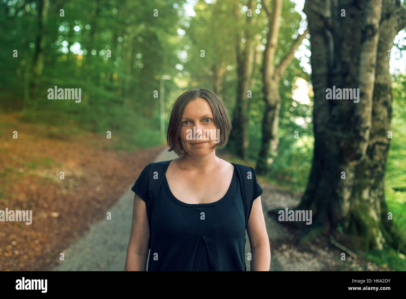 Bella giovane femmina adulta guardando la fotocamera in boschi, escursionismo donna con uno zaino che pongono in posizione di parcheggio o di una foresta Foto Stock