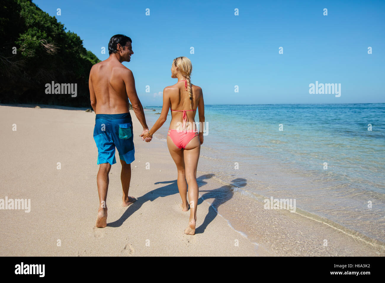 Luna di Miele giovane holding hands camminando sulla riva del mare. Matura in amore su rilassanti vacanze estive sulla spiaggia. Vista posteriore shot. Foto Stock