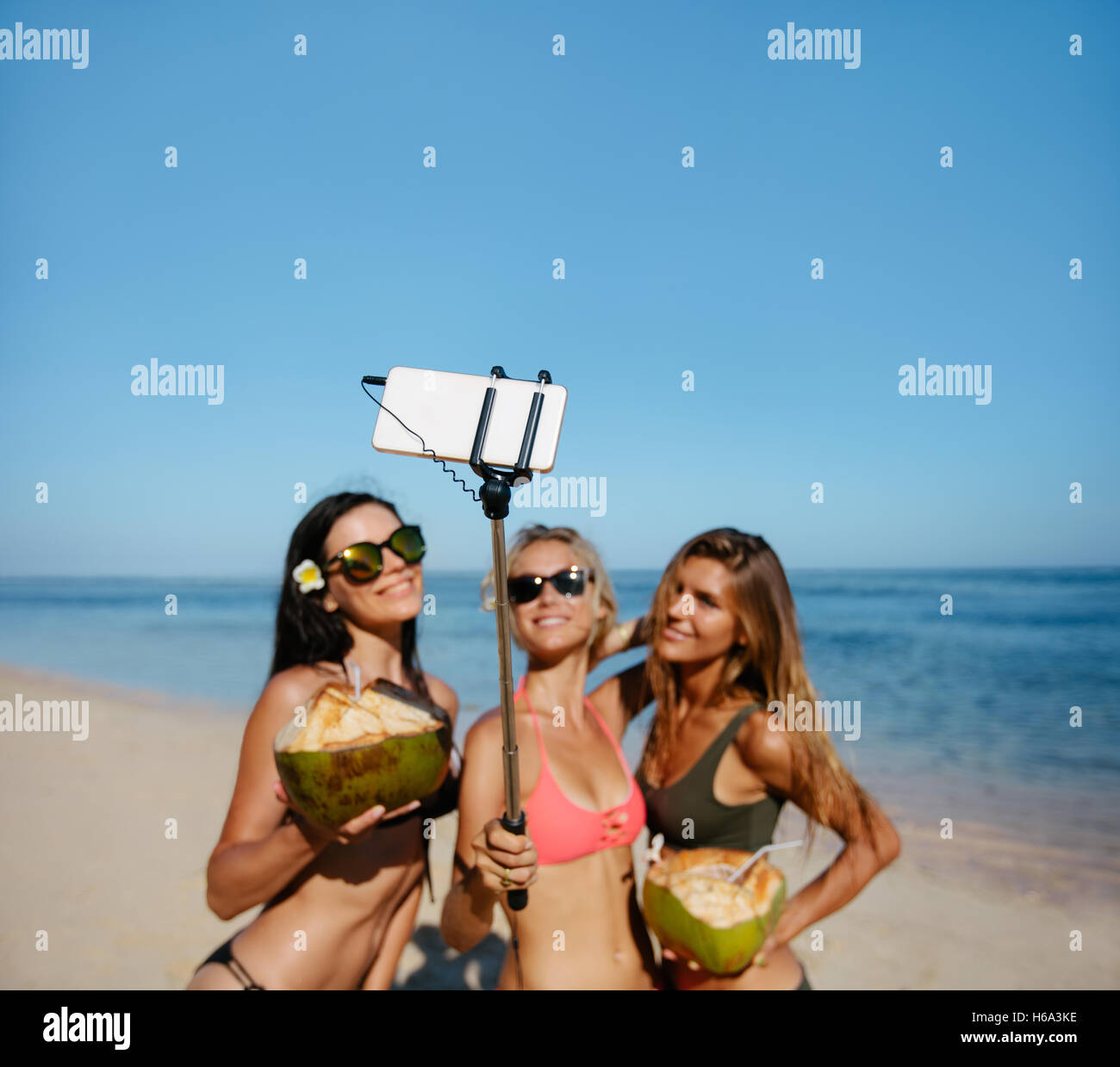 Tre giovani donne in bikini sulla spiaggia prendendo autoritratto con smart phone su selfie stick. Il gruppo di amici di sesso femminile holding Foto Stock