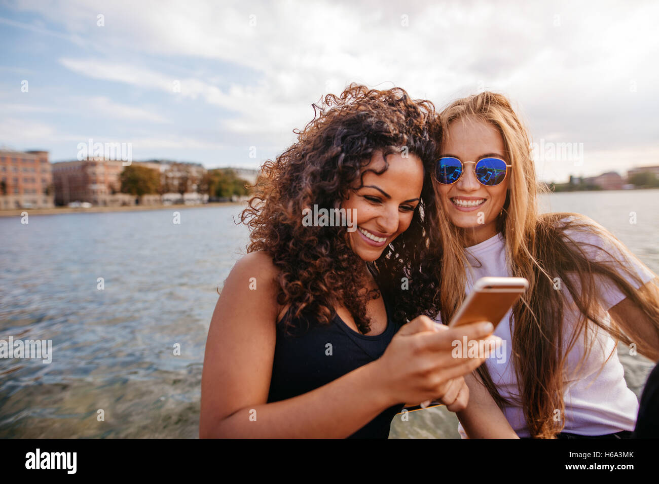 Colpo di due giovani donne alla ricerca al telefono cellulare. Amici di sesso femminile utilizzando smart phone dal lago. Foto Stock