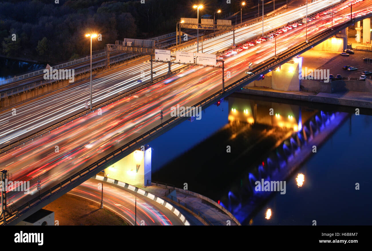 Ponte stradale sul fiume di notte, vista da sopra. sentieri di luce di vetture su una autostrada. Inceppamento di traffico su una lunga esposizione Foto Stock