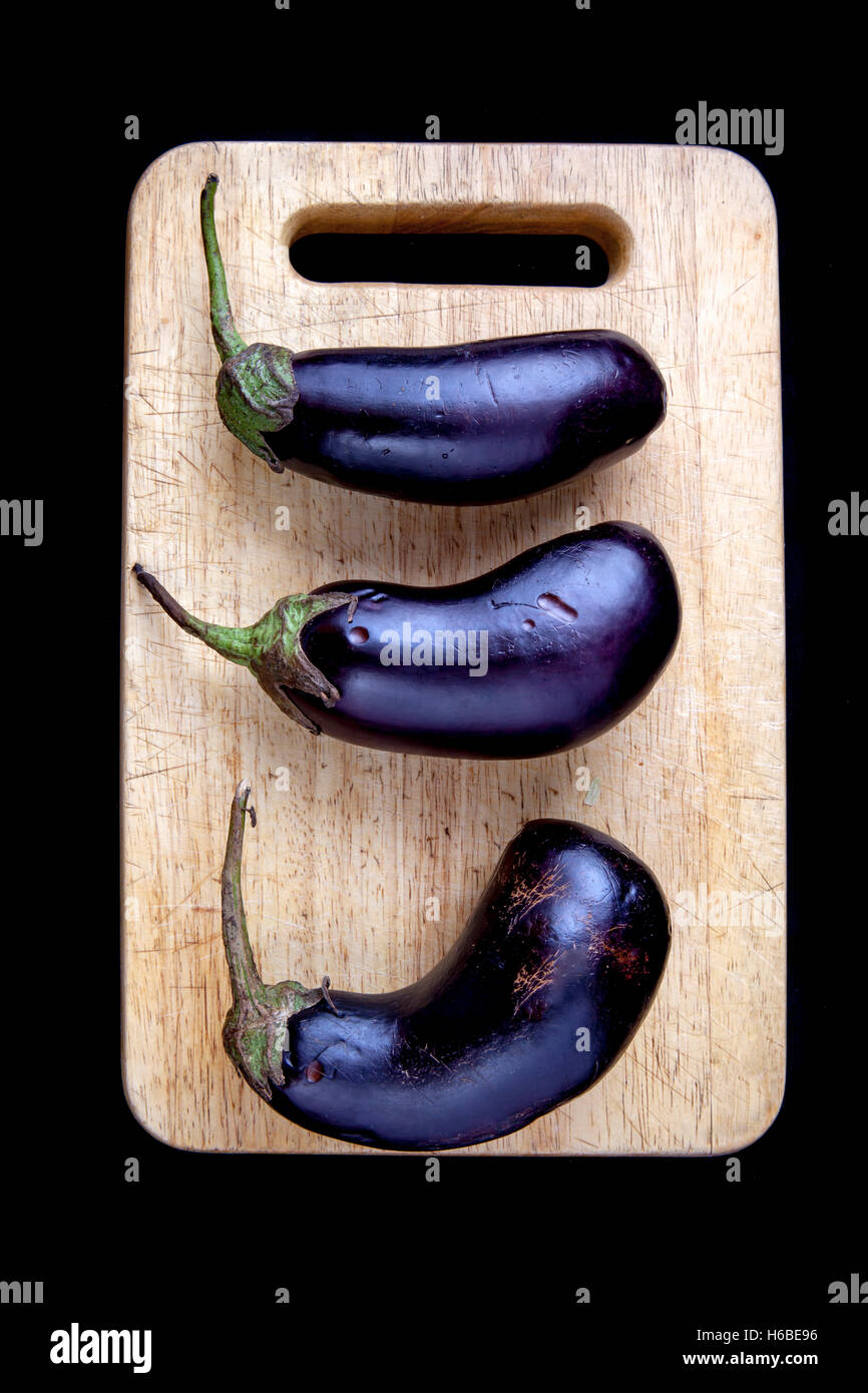 Organico sano melanzana, giacente su una tavola di legno isolato su sfondo nero Foto Stock