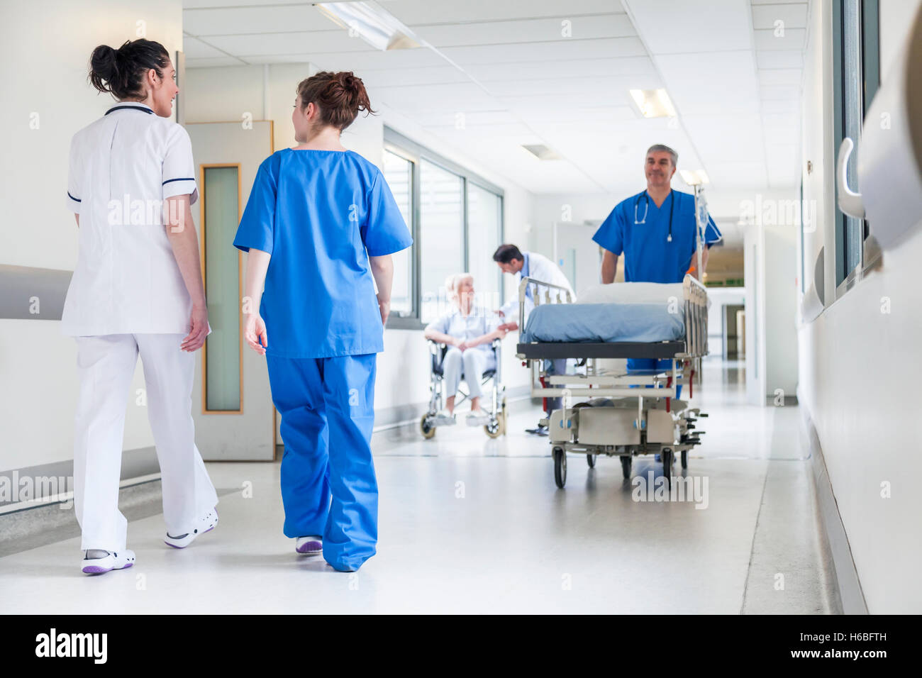 Infermiere spingendo barella barella letto nel corridoio di ospedale con medici & senior paziente femmina Foto Stock