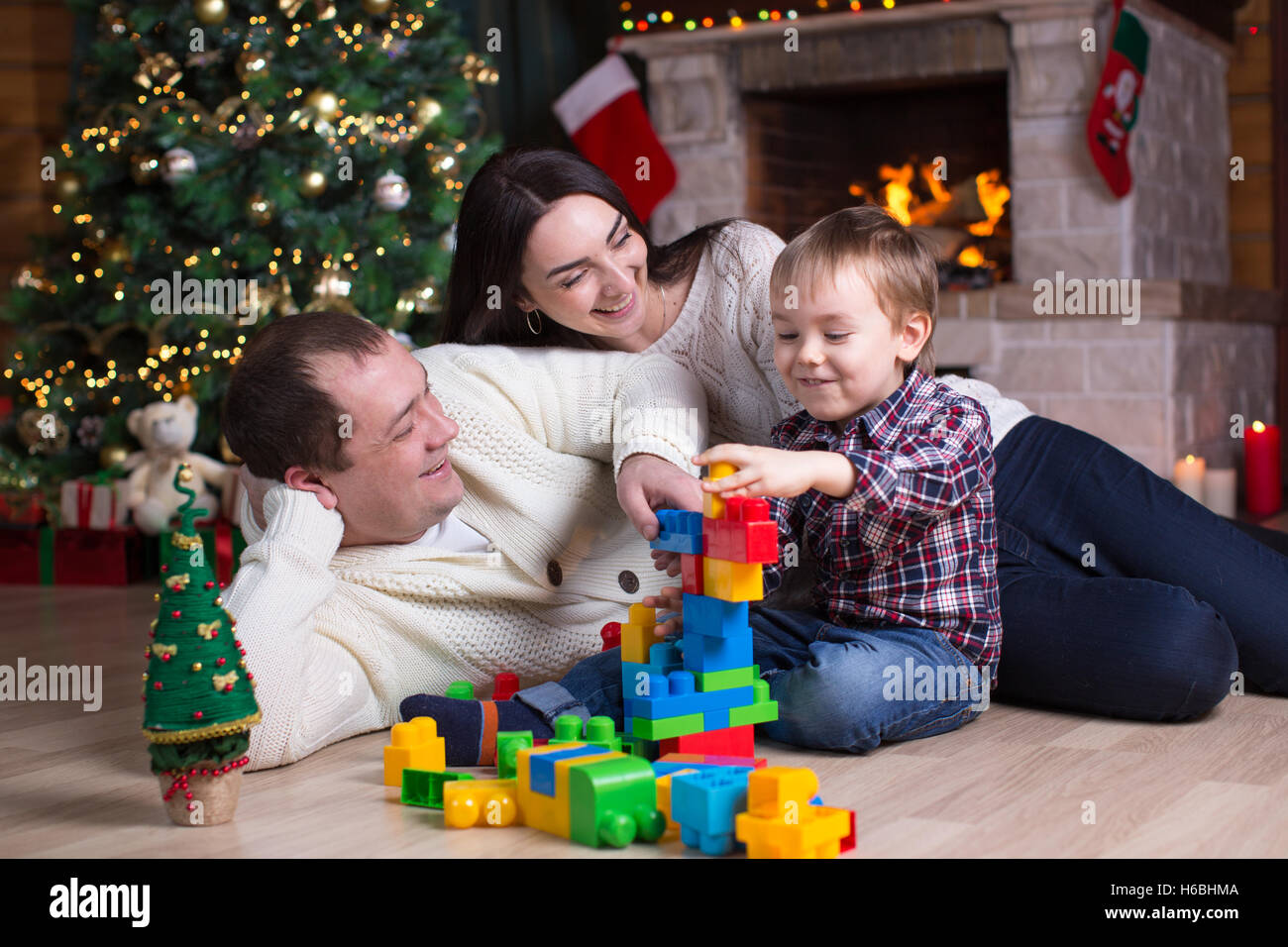 Kid boy e i suoi genitori a giocare con i giocattoli di blocco sotto l'albero di natale Foto Stock