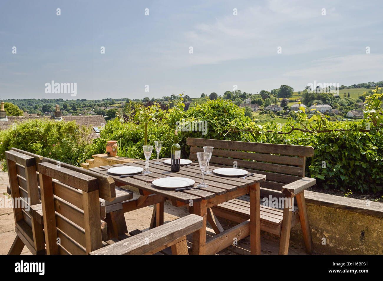 Un tavolo da giardino e sedie con luogo settings & vino per un pasto con vista sulle colline di Cotswold a Nailsworth, Regno Unito Foto Stock