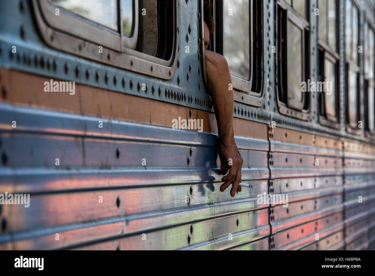 Incollaggio a mano al di fuori della finestra del treno con la sigaretta in esso, e colori che riflettono off treno auto. Foto Stock