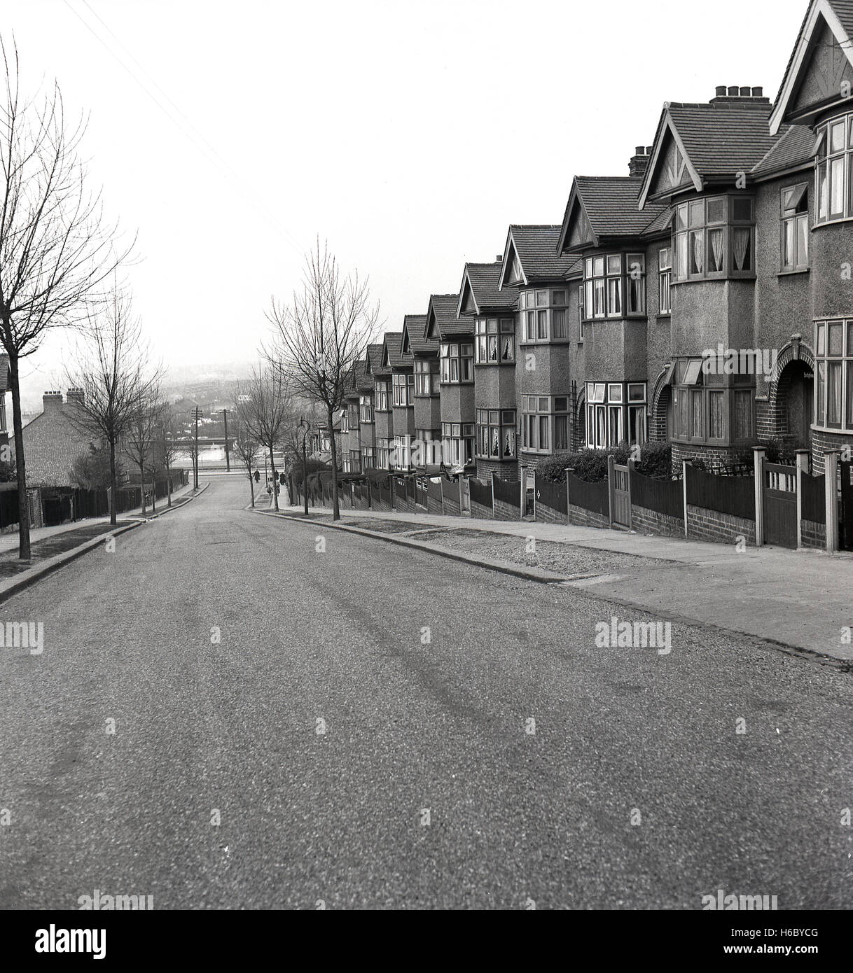 Degli anni Cinquanta, storico, vista esterna di una tranquilla strada di Londra che mostra una fila di trenta interwar Pebble Dash suburbana di case a schiera costruito su una collina. Una moto e sidecar è visibile nella parte anteriore di uno. Foto Stock