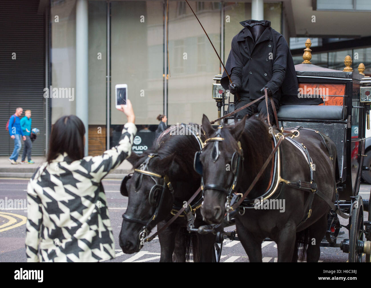 Una donna scatta una foto di un "cavaliere senza testa" che cavalcava una carrozza trainata da cavalli attraverso il centro di Londra per promuovere una serie di "passeggiate di cura" di Halloween che si svolgono intorno a Holborn e Bloomsbury dal 28 al 31 ottobre. Foto Stock