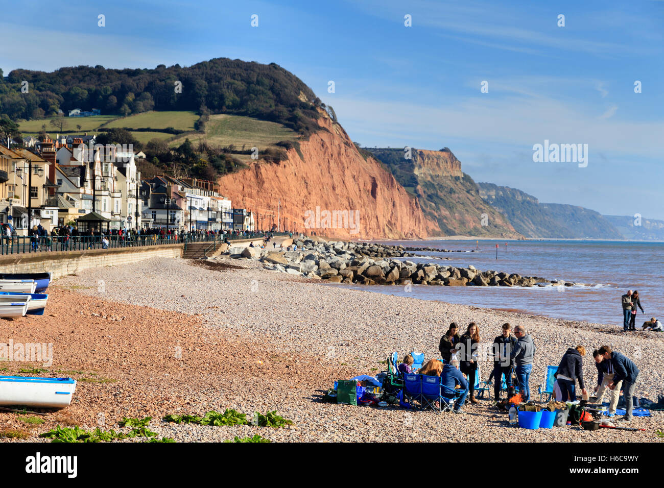 Visitatori godendo di fine ottobre sole sulla spiaggia a Sidmouth, nel Devon, Regno Unito. Città, Esplanade e la Jurassic Coast scogliere in background Foto Stock