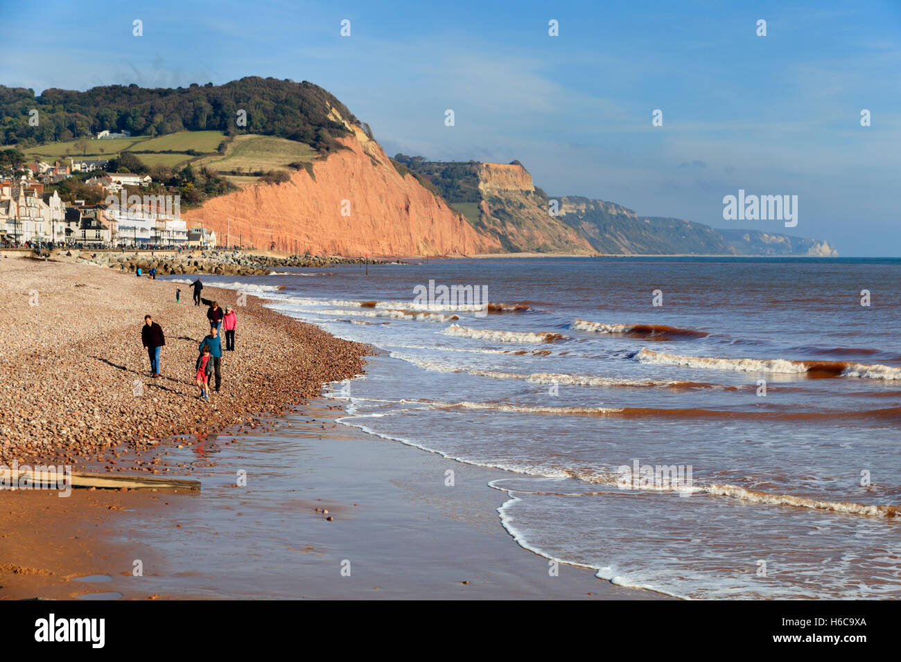 Visitatori godendo di fine ottobre sole sulla spiaggia a Sidmouth, nel Devon, Regno Unito. Città, Esplanade e la Jurassic Coast scogliere in background Foto Stock
