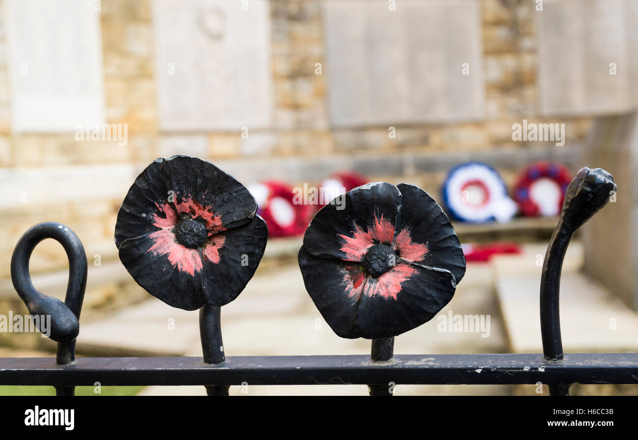 Close up di nero ferro battuto ringhiera decorativo in forma di un papavero attorno ad un memorial, con semi di papavero ghirlande dietro Foto Stock