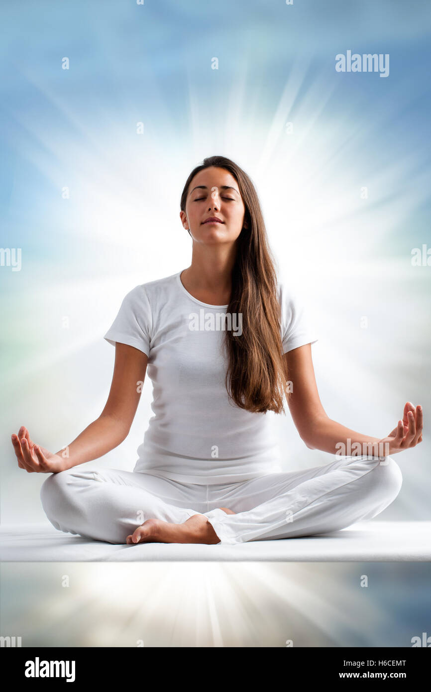 Close up ritratto di attraente giovane donna meditando con gli occhi chiusi. Vista frontale della donna vestita di bianco in posizione di yoga. Foto Stock