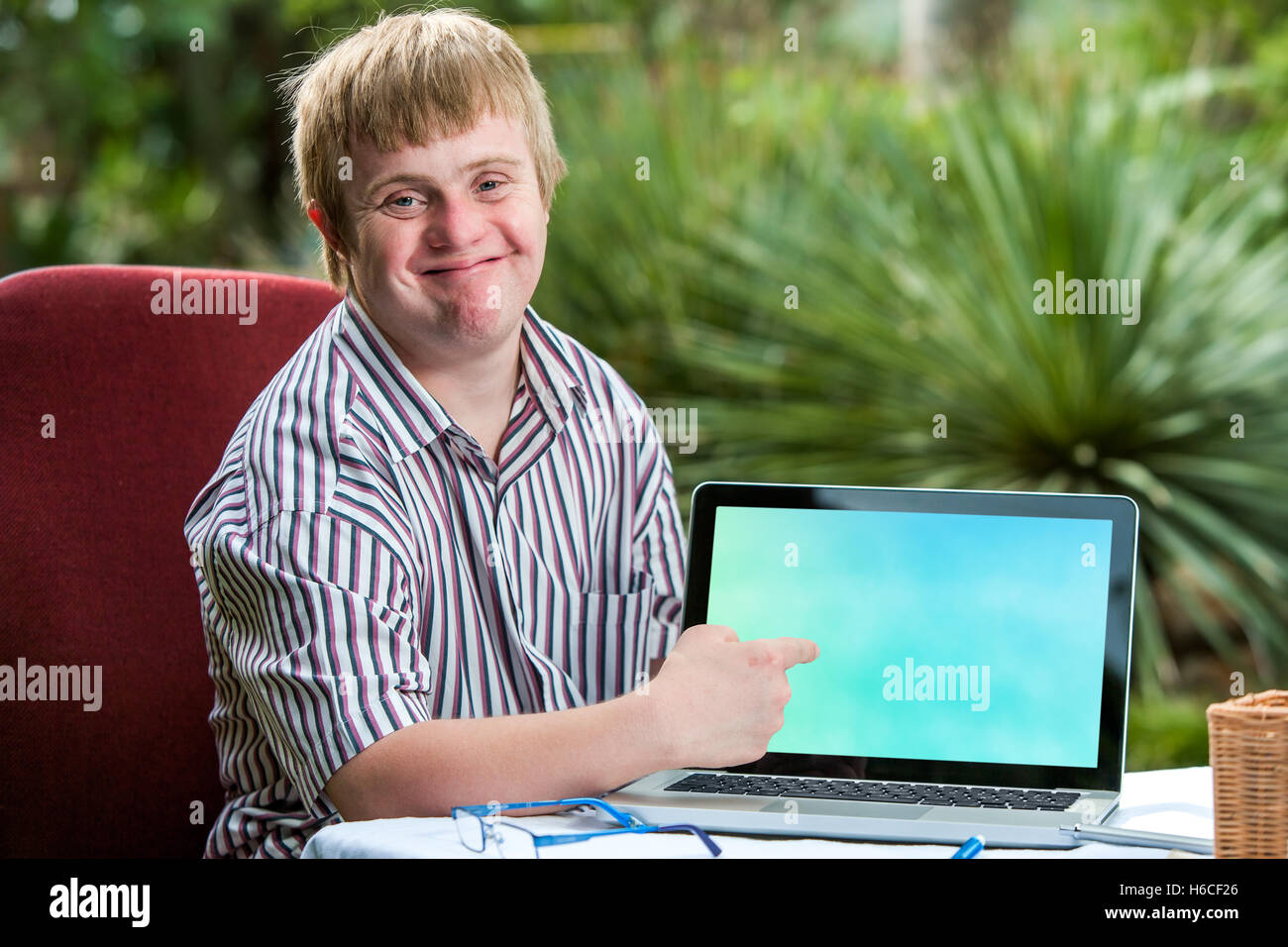 Close up ritratto di cordiale giovane studente con la sindrome di down rivolto a vuoto allo schermo del laptop.seduto alla scrivania in giardino. Foto Stock
