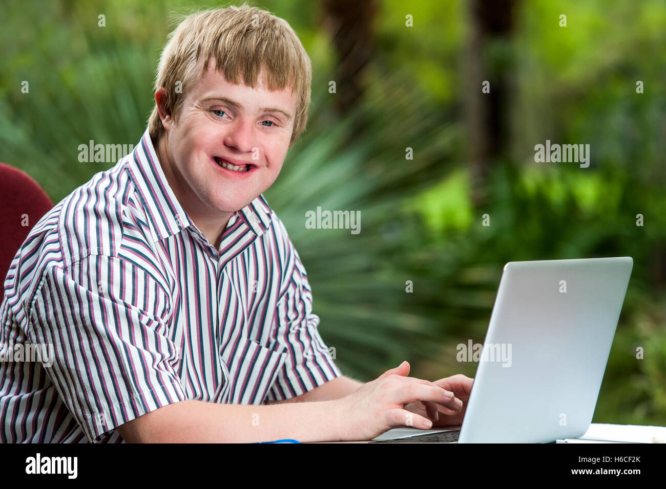 Ritratto di felice handicappati giovane digitando su laptop in giardino. Foto Stock