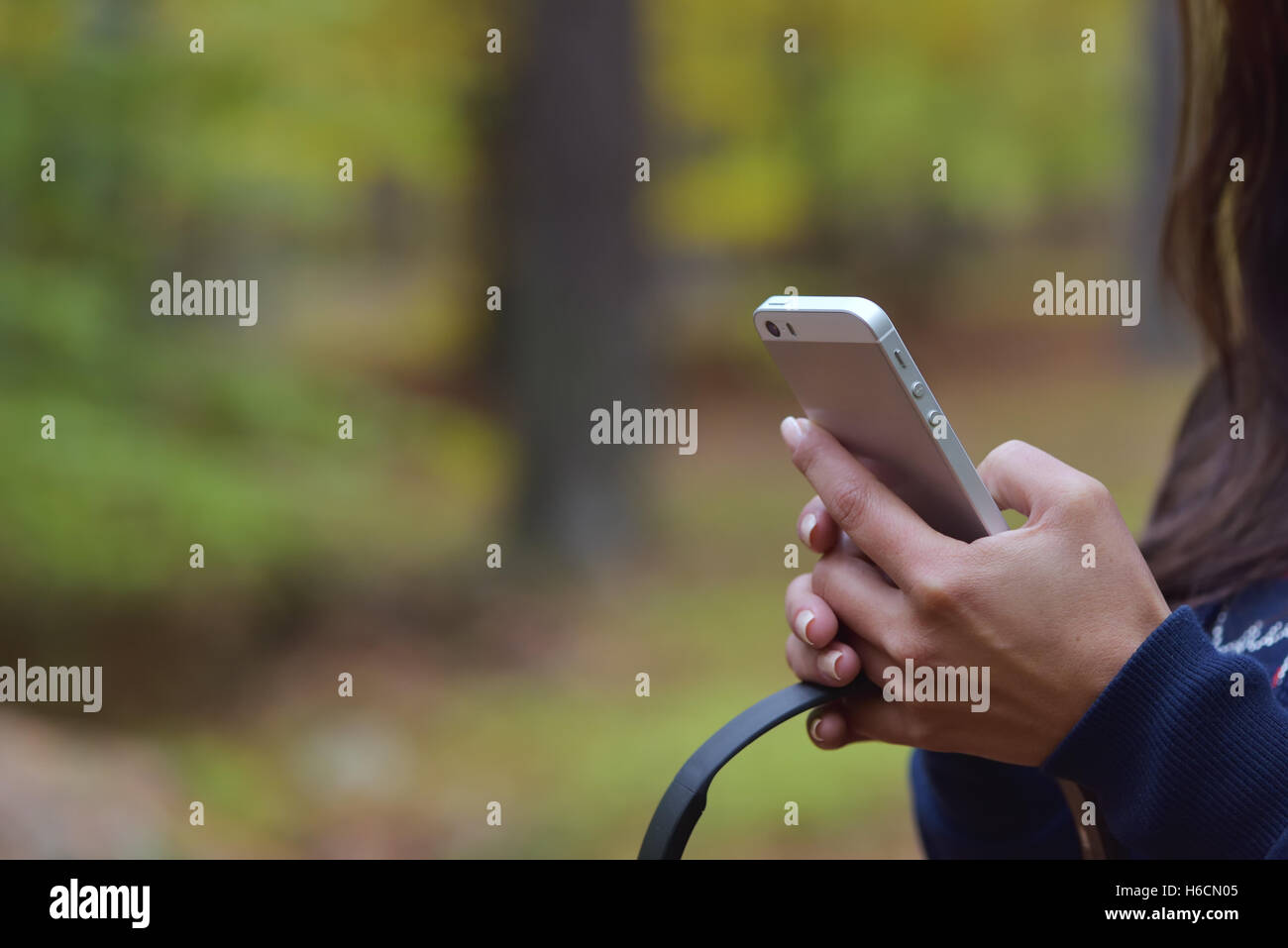 Donna che mantiene il telefono cellulare e le cuffie in mano contro un sfocata autunno sfondo forrest Foto Stock