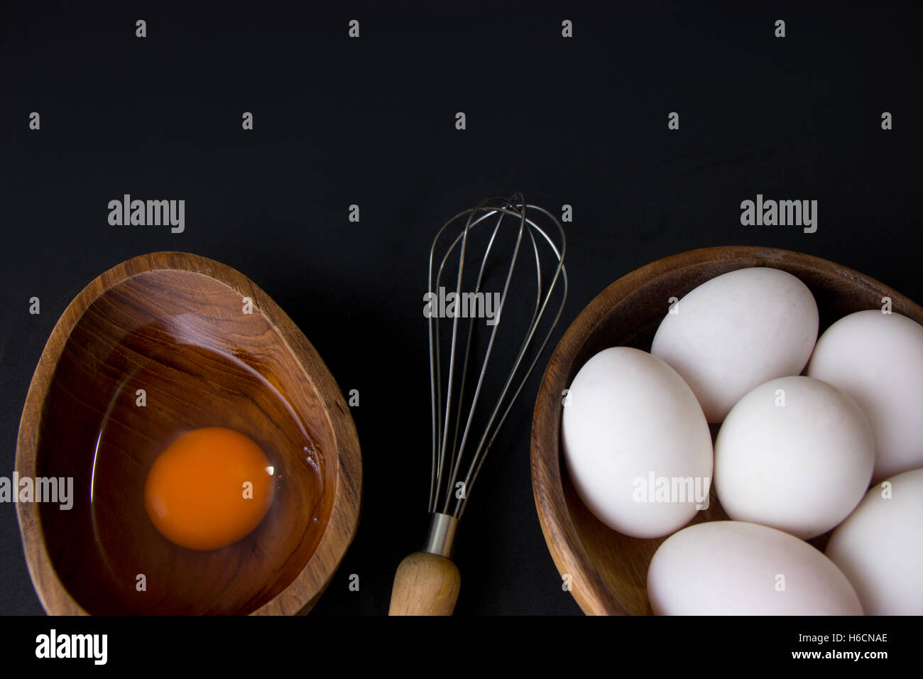 Uovo bianco in legno di teak ciotola e mescolare con una frusta su sfondo nero Foto Stock