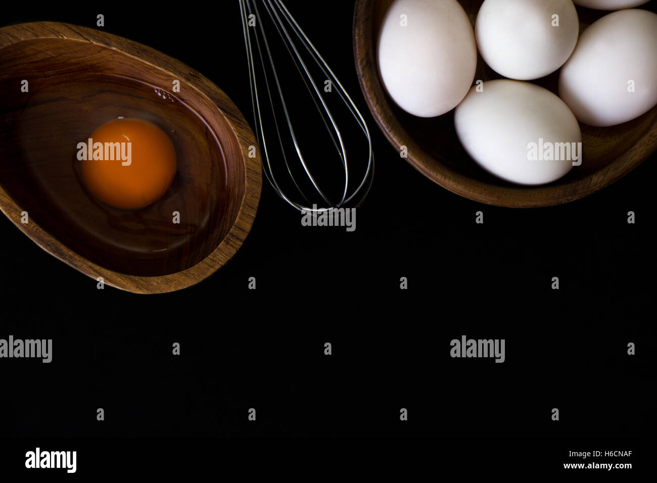 Uovo bianco in legno di teak ciotola e mescolare con una frusta su sfondo nero Foto Stock