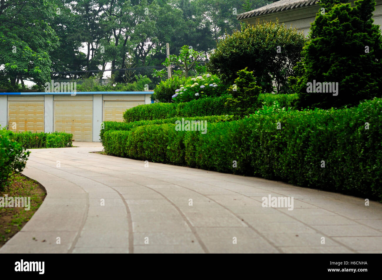 Un lungo viale di accesso ed è circondata da piante e arbusti che termina in corrispondenza di tre porte di garage a Qingdao in Cina. Foto Stock