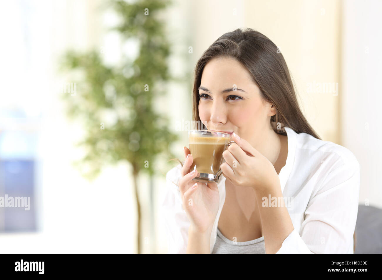 Donna sorseggiando e bere un delizioso caffè con il latte che guarda lontano da casa Foto Stock