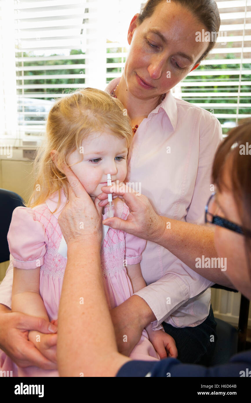 Bambino di 2 anni con la mamma / madre, riceve la dose di Fluenz vaccino antinfluenzale spray nasale immunizzazione dalla pratica di NHS nurse REGNO UNITO Foto Stock